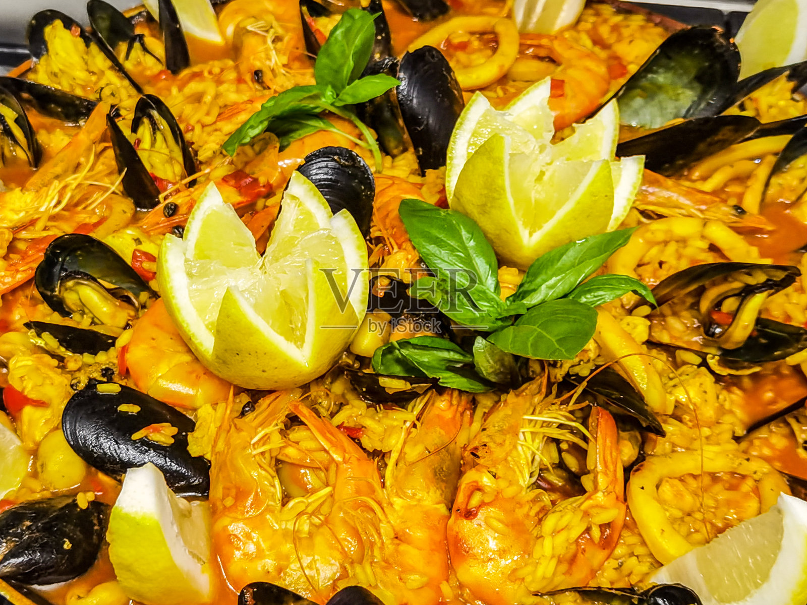 家庭式海鲜饭，以虾、贻贝、柠檬和罗勒为装饰。照片摄影图片