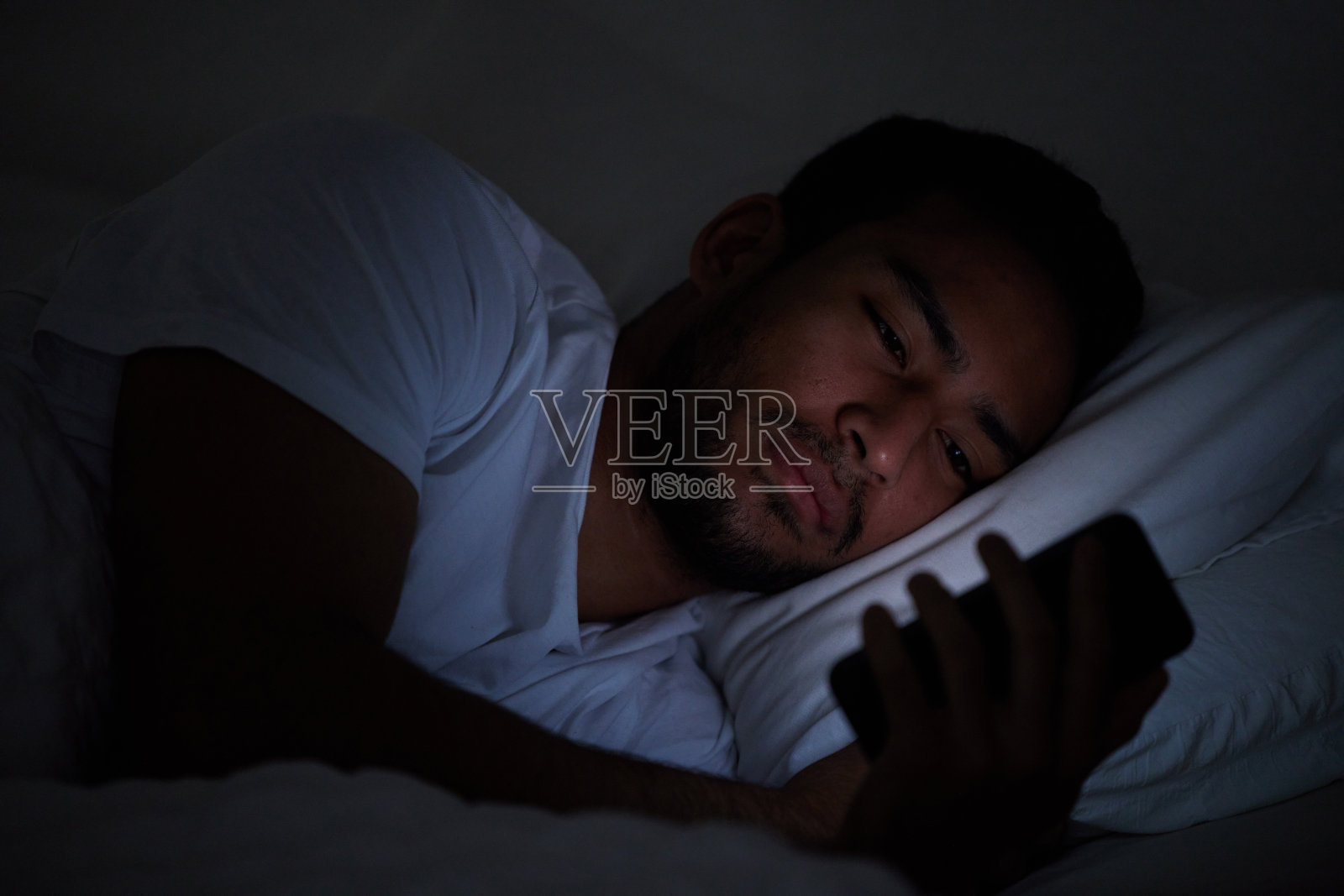 一名男子晚上躺在床上使用手机的镜头照片摄影图片