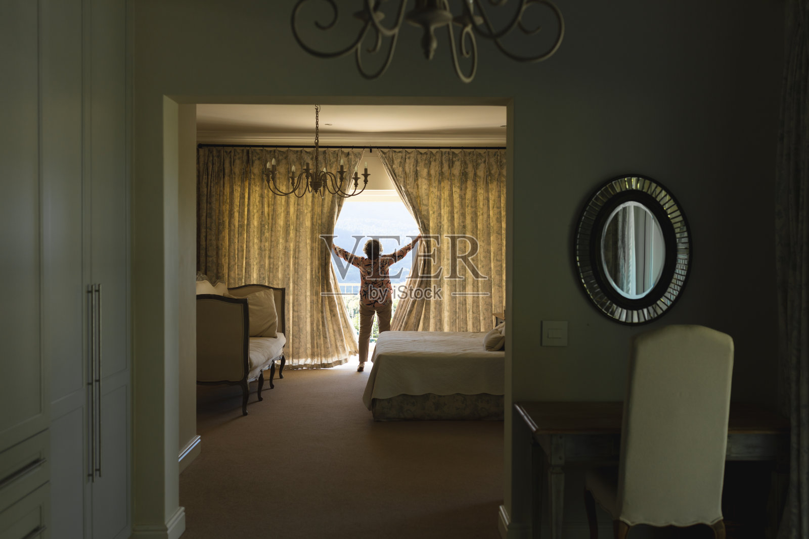 一个白人老太太站在卧室的窗帘旁边照片摄影图片