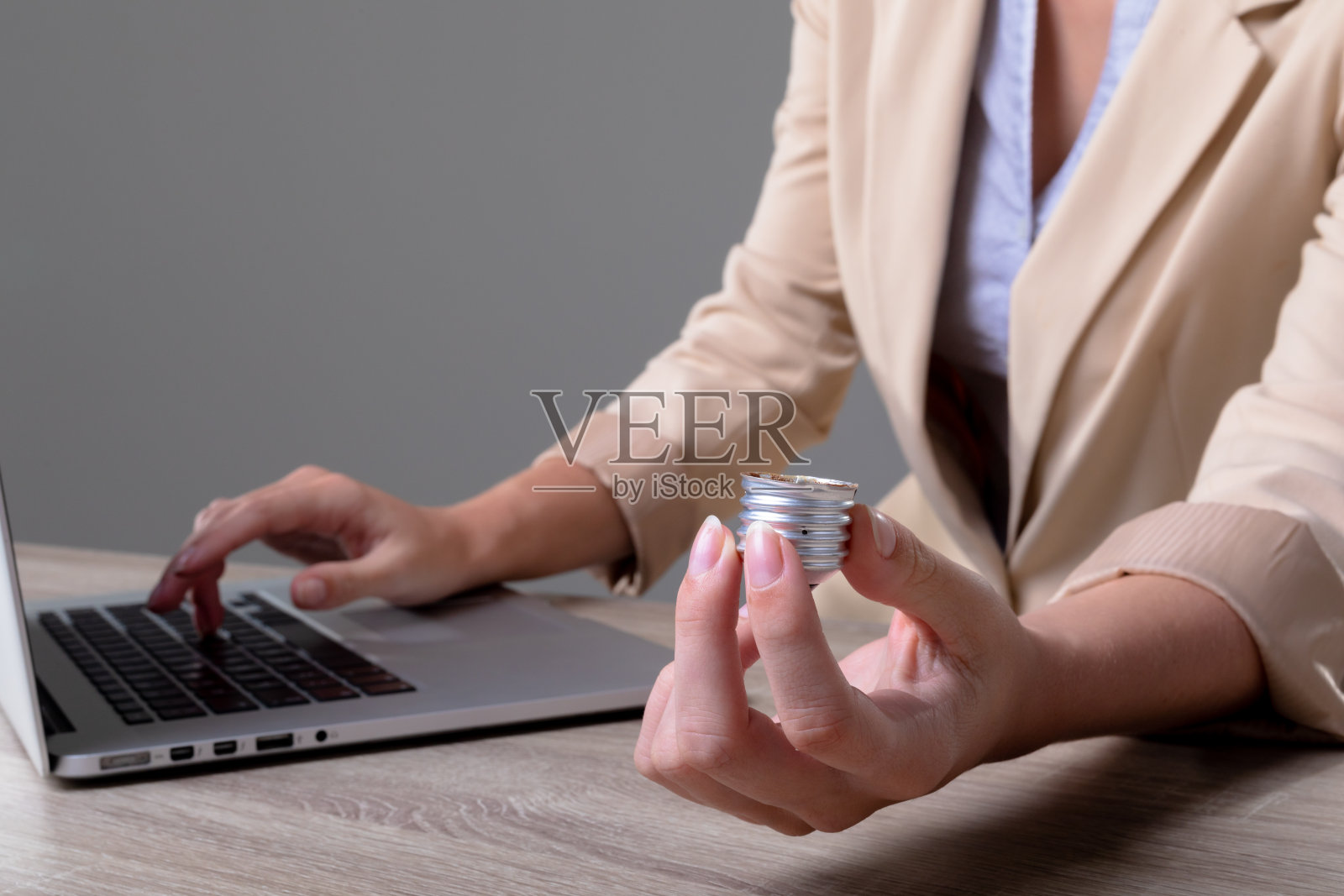 拿着灯泡底部的白人女商人，灰色背景照片摄影图片