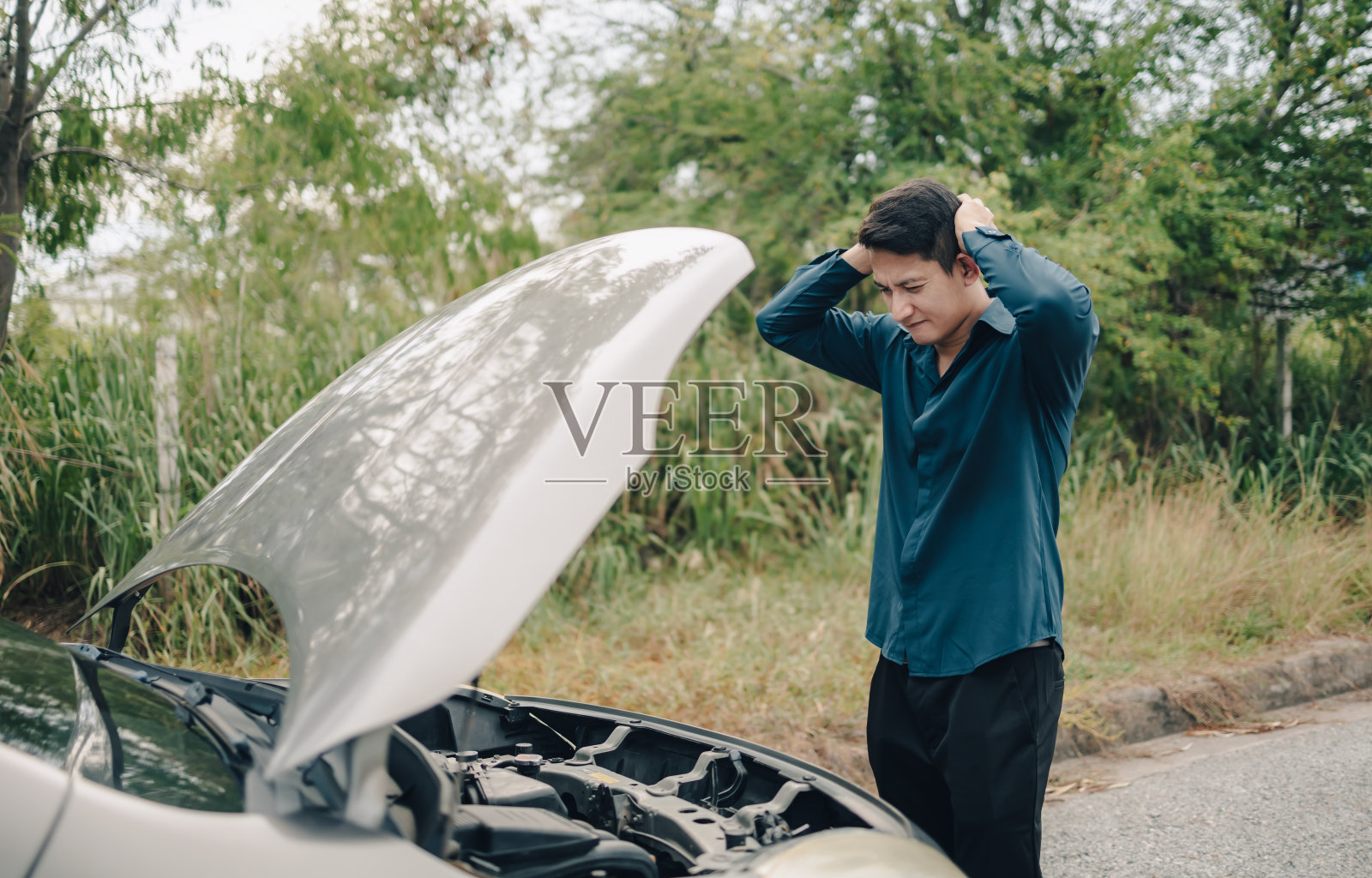 严重的男人头痛前面的汽车故障和打开引擎盖在路边。车坏了的概念。照片摄影图片