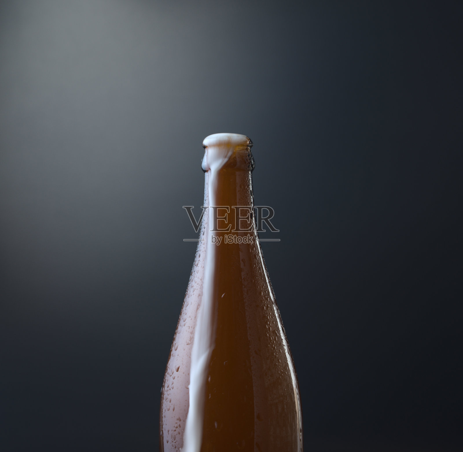 前视图一瓶冰啤酒与溢出的泡沫对深蓝色垃圾背景。冷酒精饮料，国际啤酒日概念。有机的摄影风格。照片摄影图片