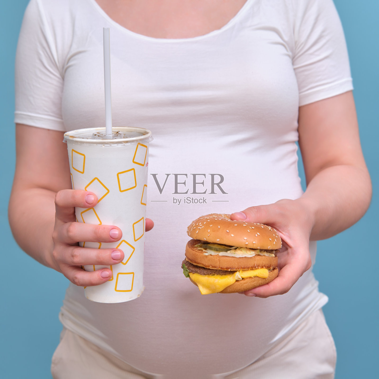 蓝色背景下一个拿着汉堡和苏打水的孕妇，特写照片摄影图片