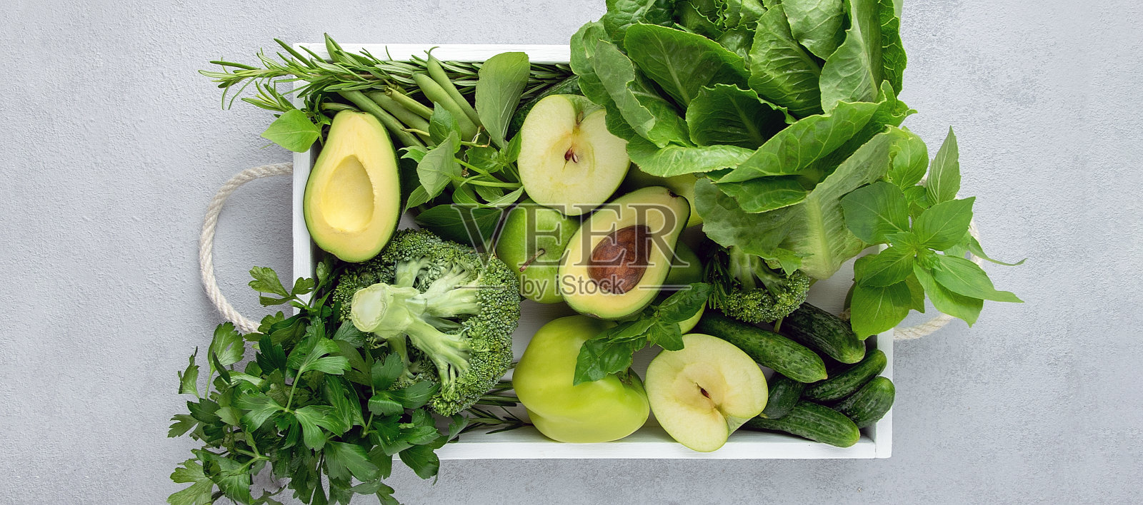 新鲜的有机绿色蔬菜和水果在托盘上的灰色背景，俯视图。横幅。照片摄影图片