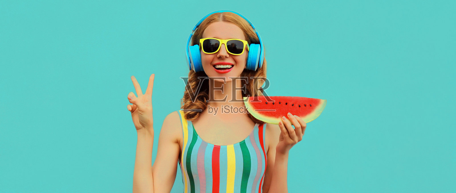 夏天的彩色肖像欢快的快乐微笑的年轻女子模特在耳机听音乐与多汁的西瓜片在蓝色的背景照片摄影图片