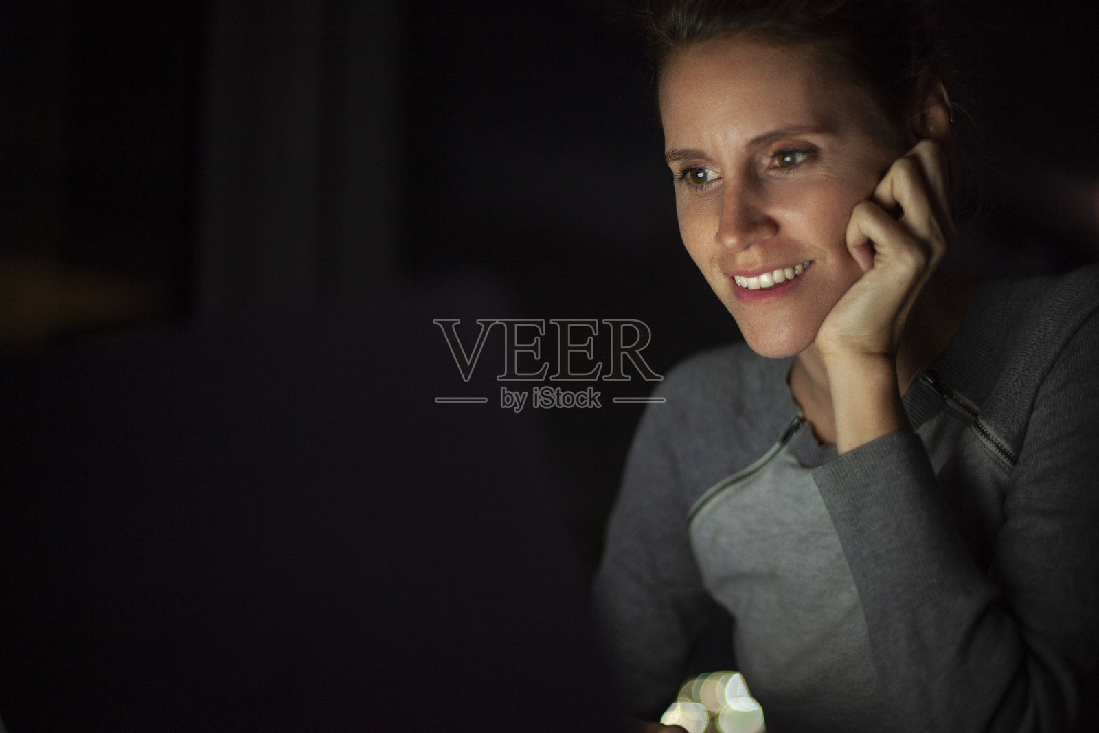 放松的中年妇女在夜间看笔记本电脑屏幕上的内容照片摄影图片