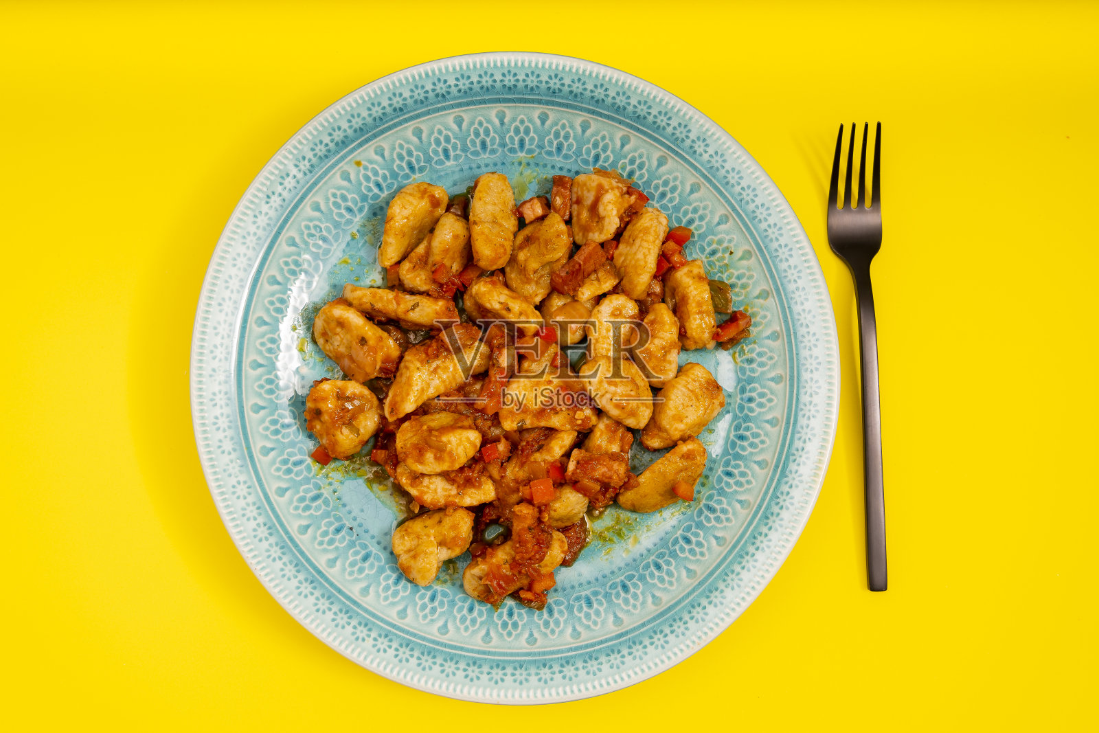 黄色的桌子上放着一盘配着红酱的意大利汤圆。搭配现代的黑色叉子。照片摄影图片