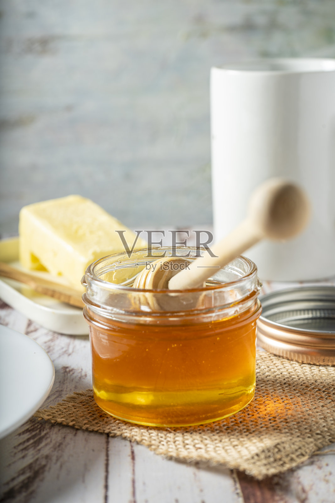 一个蜂蜜罐子的特写镜头与蜂蜜棒与自制有机黄油的背景。健康食品的概念。照片摄影图片