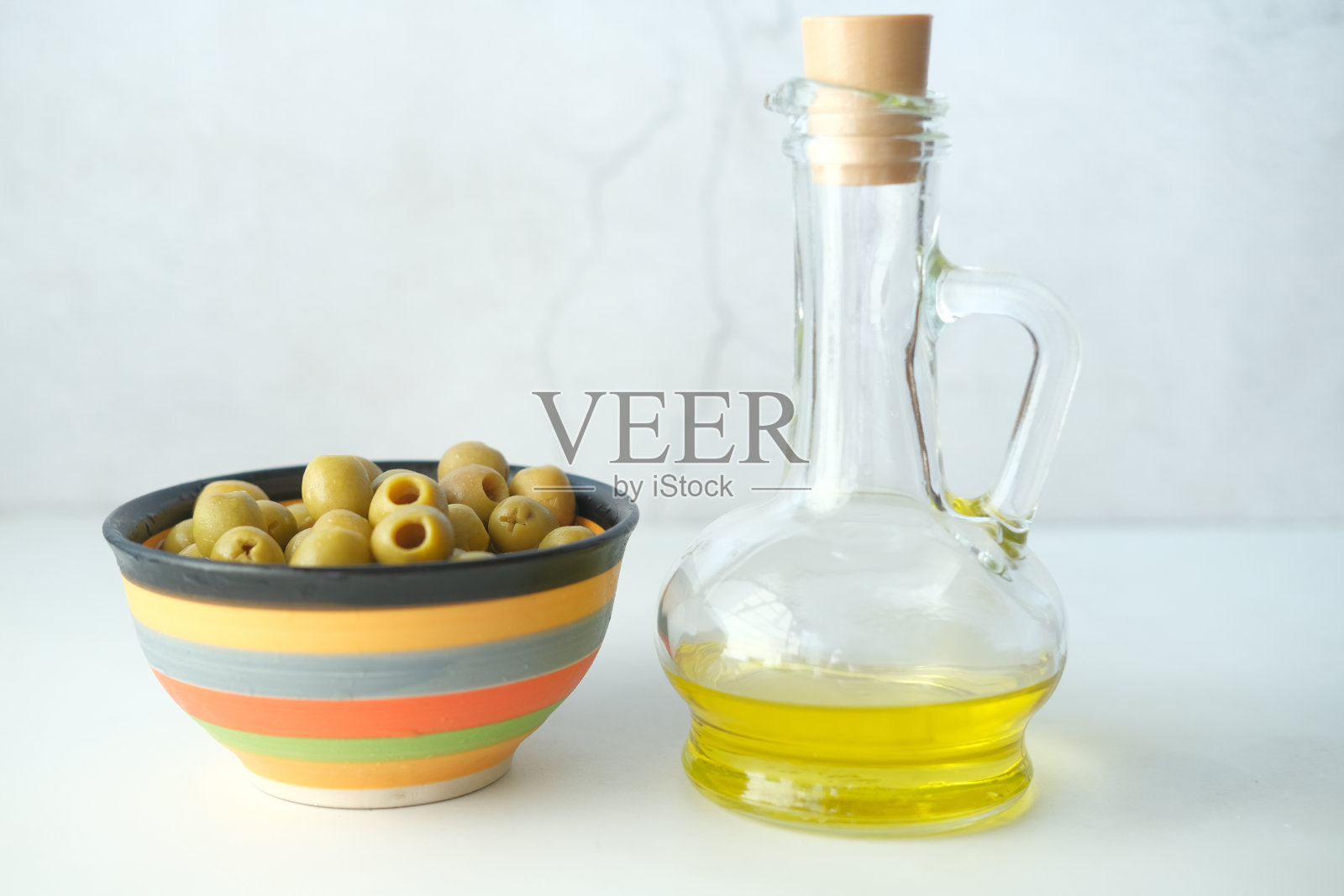 桌上的容器里装着一瓶橄榄油和新鲜橄榄。照片摄影图片