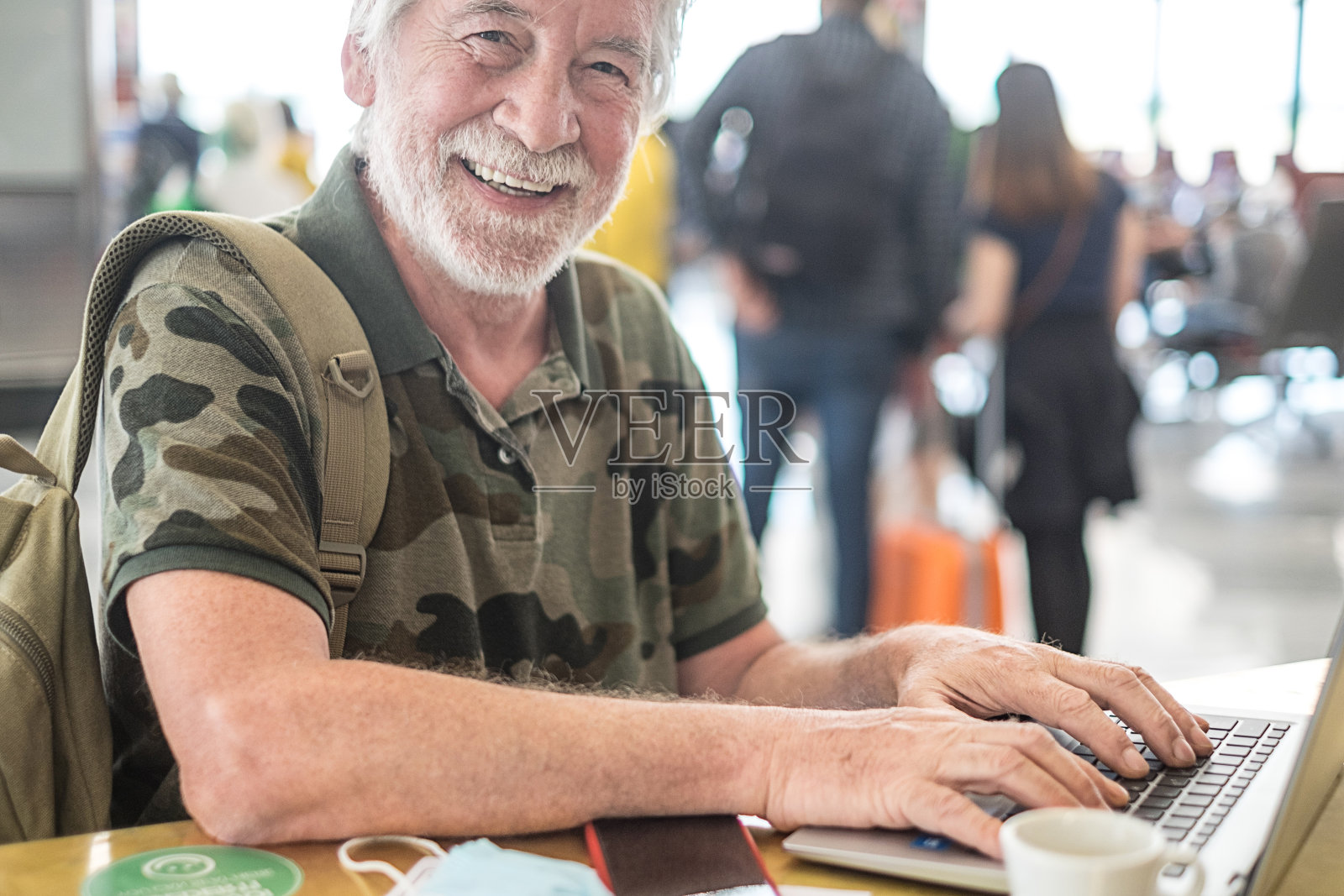 在机场等待登机的一名男子正在用笔记本电脑工作，满脸胡须的老人对着镜头微笑照片摄影图片