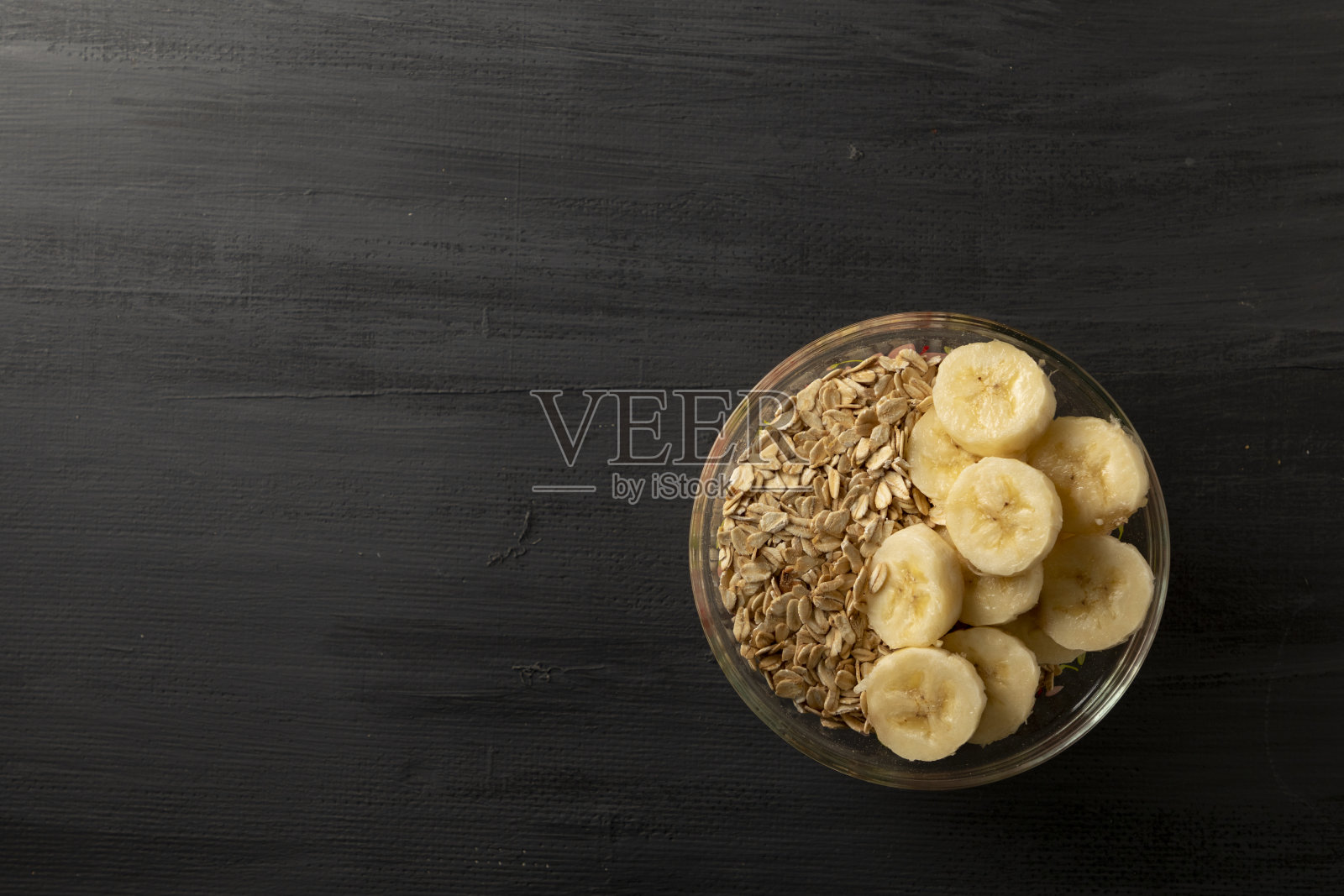 黑色的桌子上放着一碗燕麦，一杯牛奶和香蕉，这是一种健康的早餐理念。黑色食品照片摄影图片