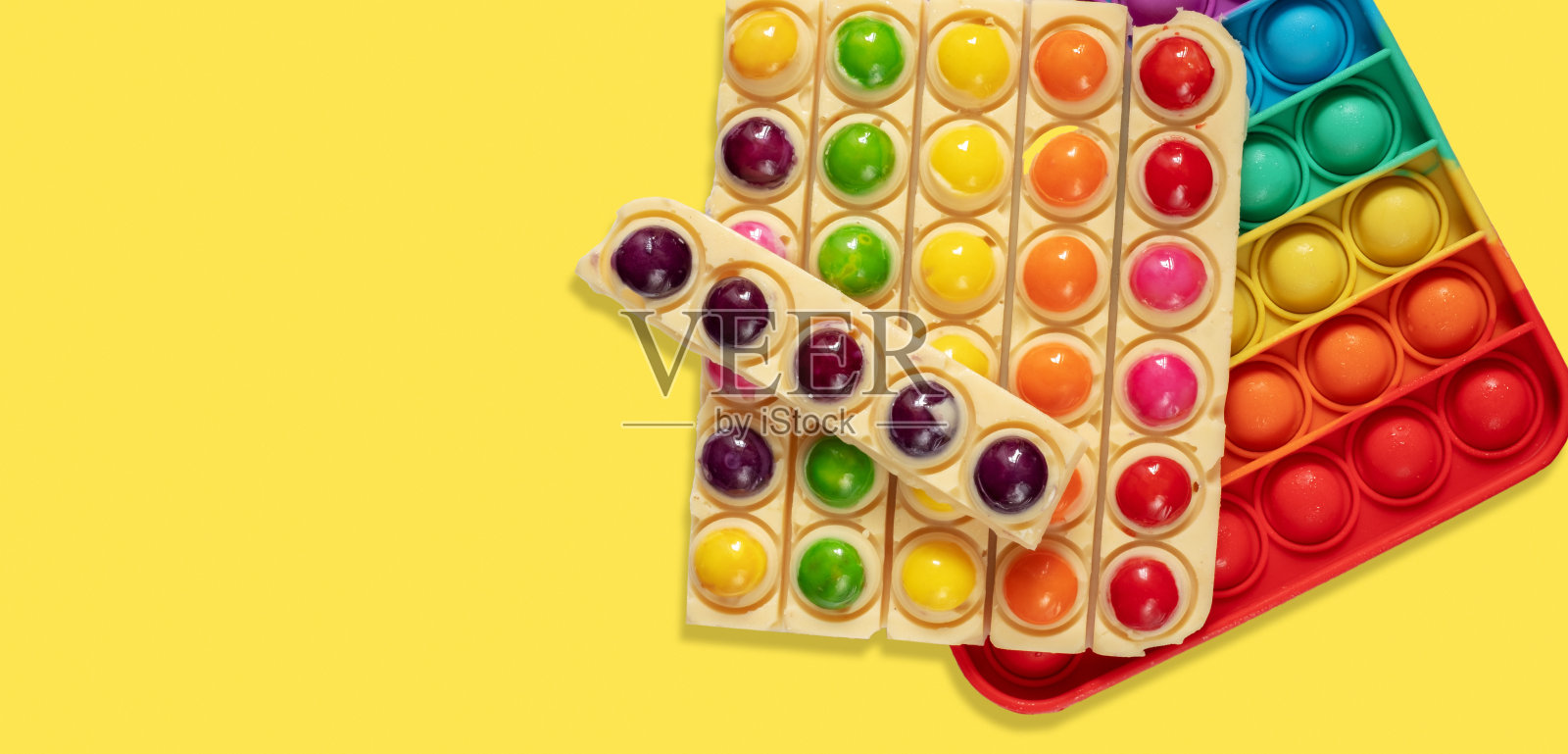 横幅。彩色糖果和白色巧克力孤立在黄色背景。用流行的玩具pop它作为一个模型的巧克力棒照片摄影图片