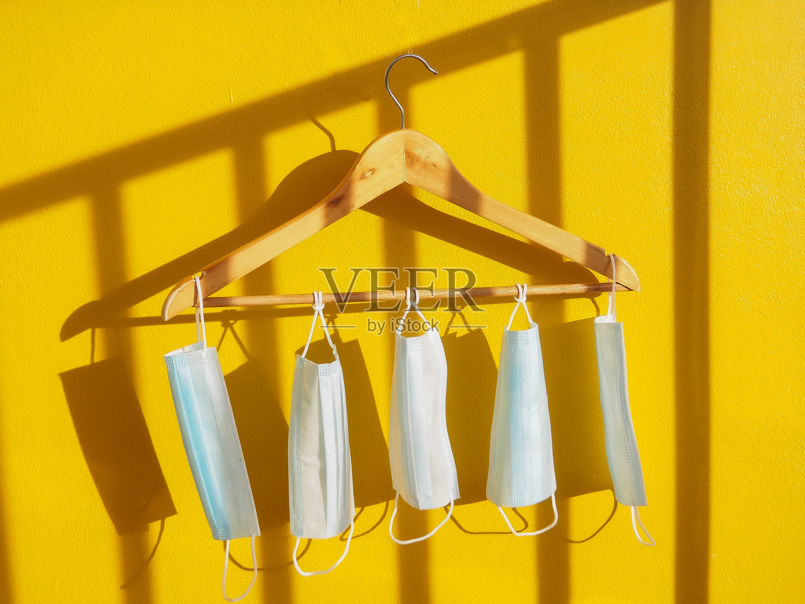 口罩或医用口罩挂在黄色背景墙上的木衣架上照片摄影图片