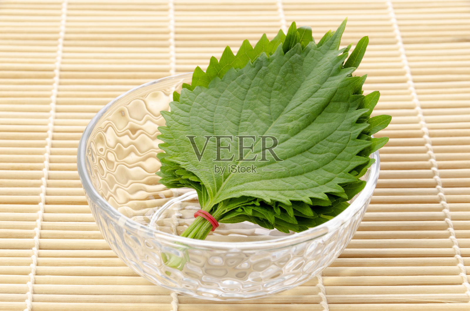 新鲜的绿色紫苏(紫苏)或欧巴叶放在一个小透明的玻璃圆碗里，放在竹滚垫上。照片摄影图片