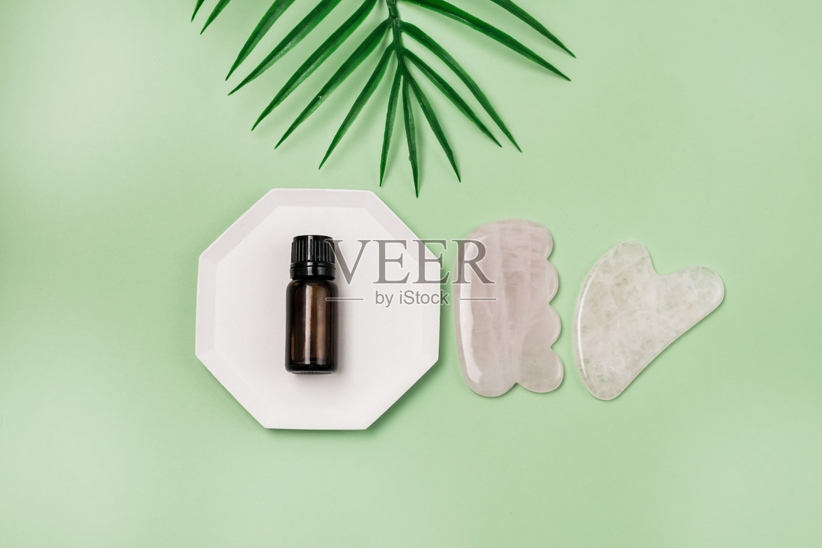 刮沙按摩器和一瓶油在绿色背景的粉红色玉石面部和身体护理水平平躺温泉最小的概念照片摄影图片