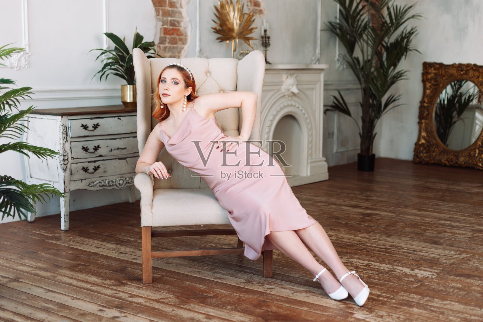 一名东欧或北欧的年轻女子穿着丝绸连衣裙，摆着美丽的姿势坐在老式的椅子上照片摄影图片