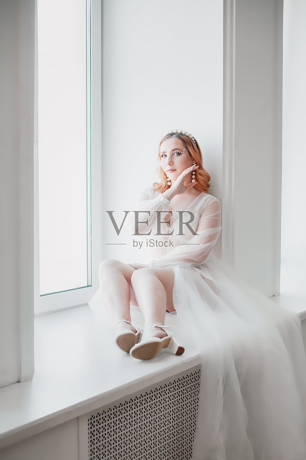 新娘穿着一件白色透明的长拖裙坐在窗台上，脚放在窗台上照片摄影图片