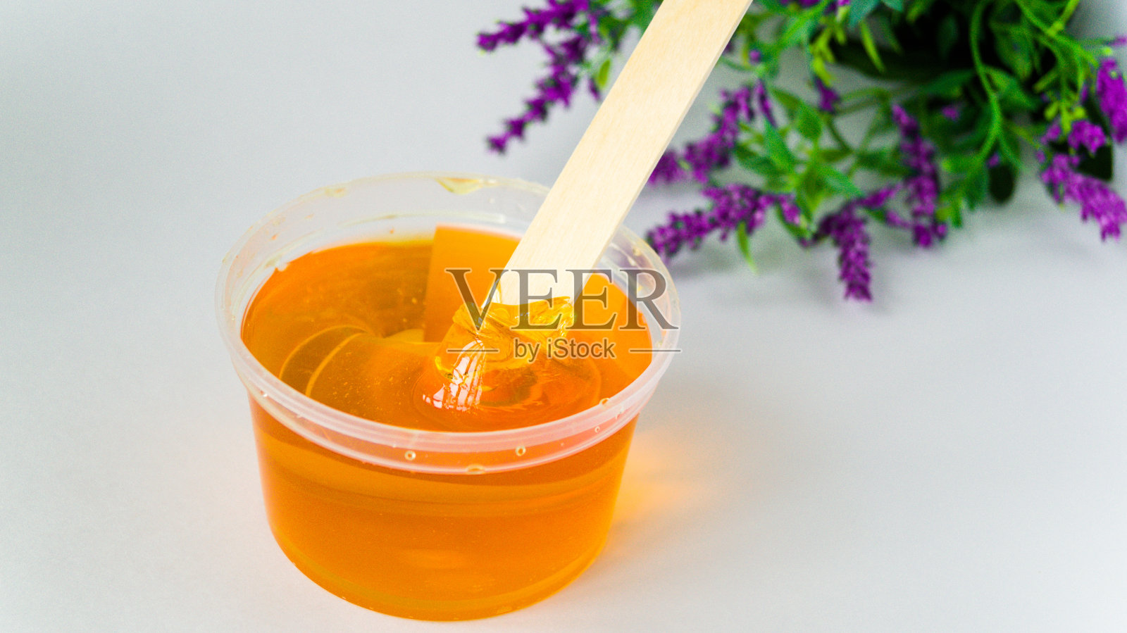 脱毛用的糖糊是用一根木头蜡棒从一个有花背景的罐子里拿出来的。照片摄影图片