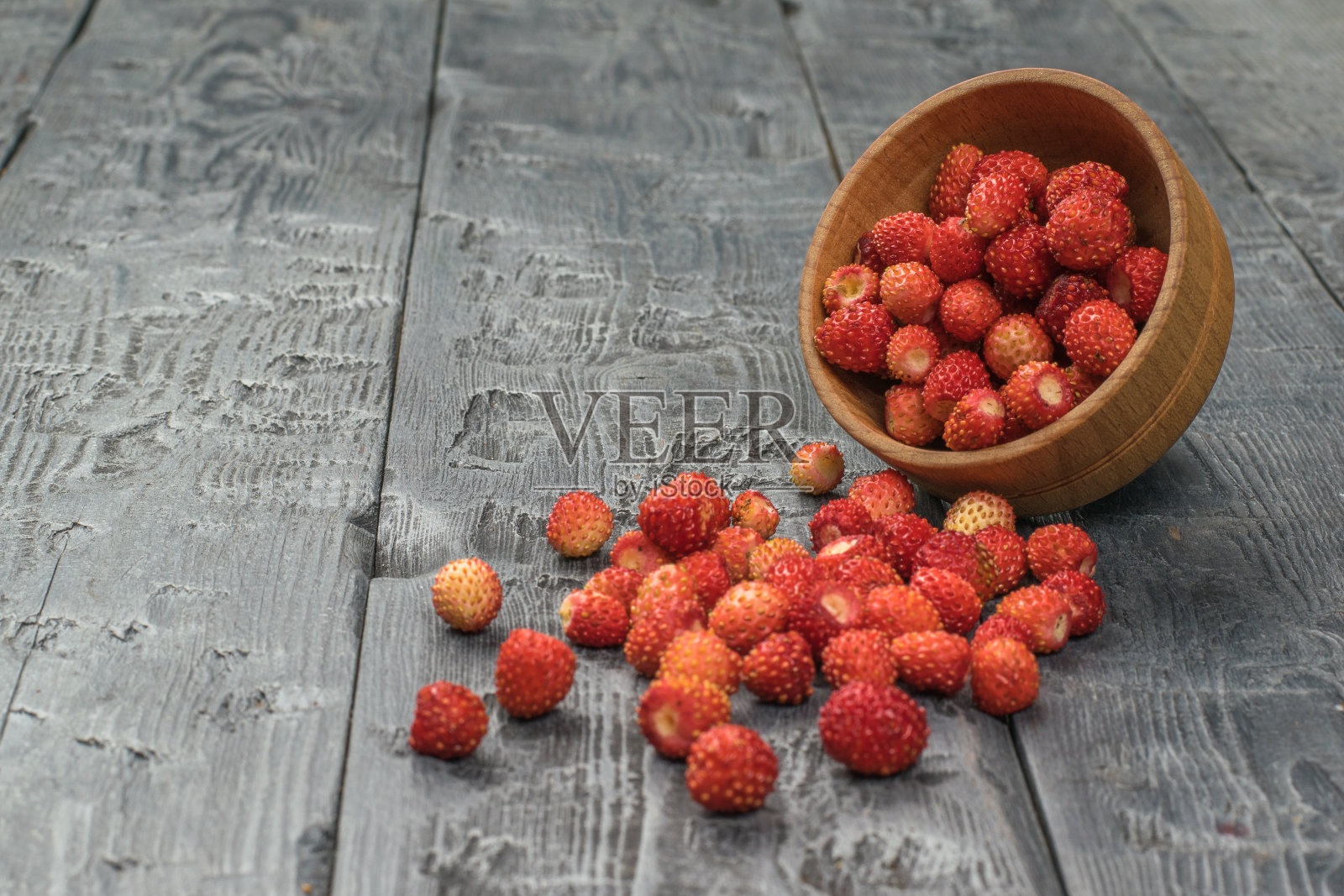 木桌上放着一只木碗，上面撒着野草莓。照片摄影图片