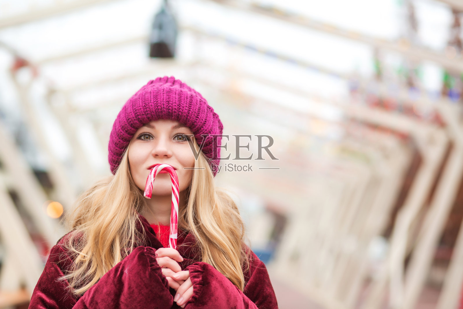 积极的金发女人在红色针织帽摆姿势与糖果手杖在街上照片摄影图片