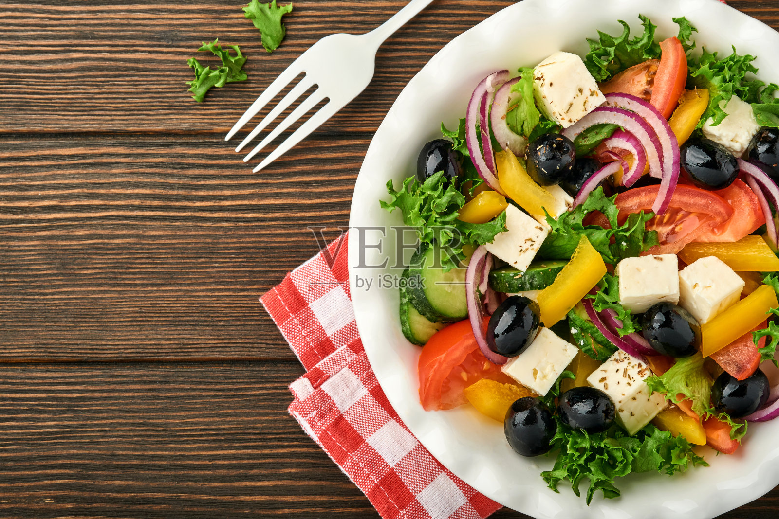 传统的希腊沙拉，用新鲜的黄瓜，番茄，甜椒，生菜，红洋葱，羊乳酪和橄榄和橄榄油放在白色的盘子里。健康食物，俯视图。照片摄影图片