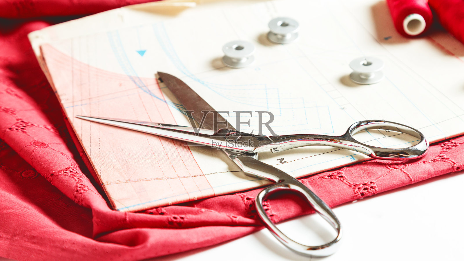时装设计师的工作空间。一张张专业的缝纫图案，卷尺，线，红色织物和剪刀照片摄影图片