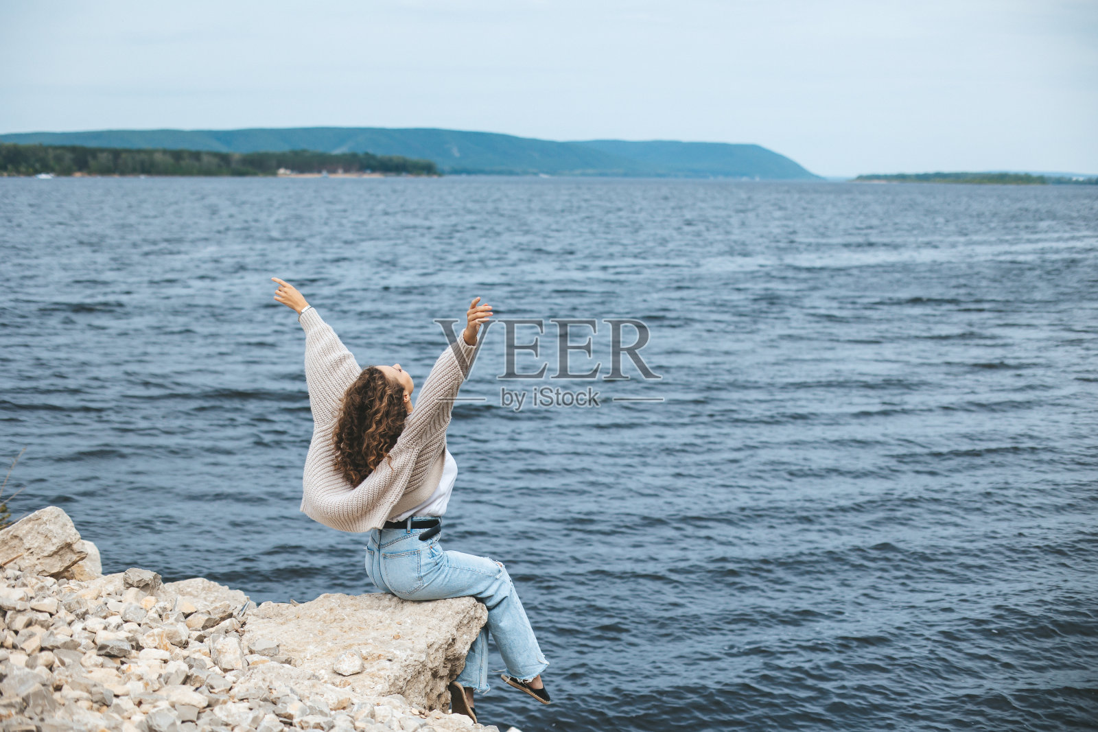 后面的年轻女子坐在岩石河岸上照片摄影图片