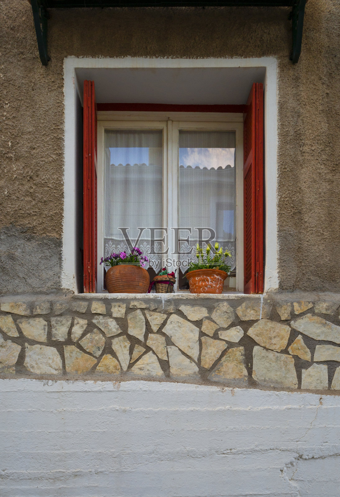 希腊阿拉科瓦市一幢漂亮的房子的窗户，有花边窗帘、鲜花和红色百叶窗照片摄影图片