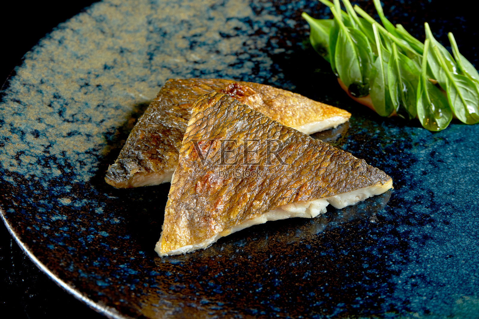 烤鲈鱼柳配菠菜及黄酱，盛于瓷盘内。食品交付。孤立在黑色照片摄影图片
