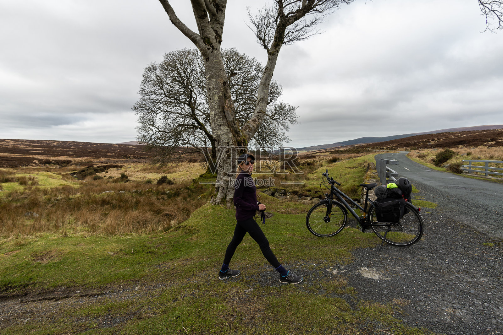 金发女人戴着眼镜，穿着运动服，骑着自行车，在树木环绕的山景中摆姿势照片摄影图片