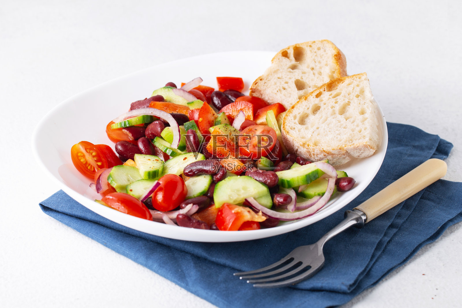 白色的盘子里有红豆和蔬菜，蓝色的餐巾，西红柿，黄瓜，洋葱，意大利脆皮面包照片摄影图片