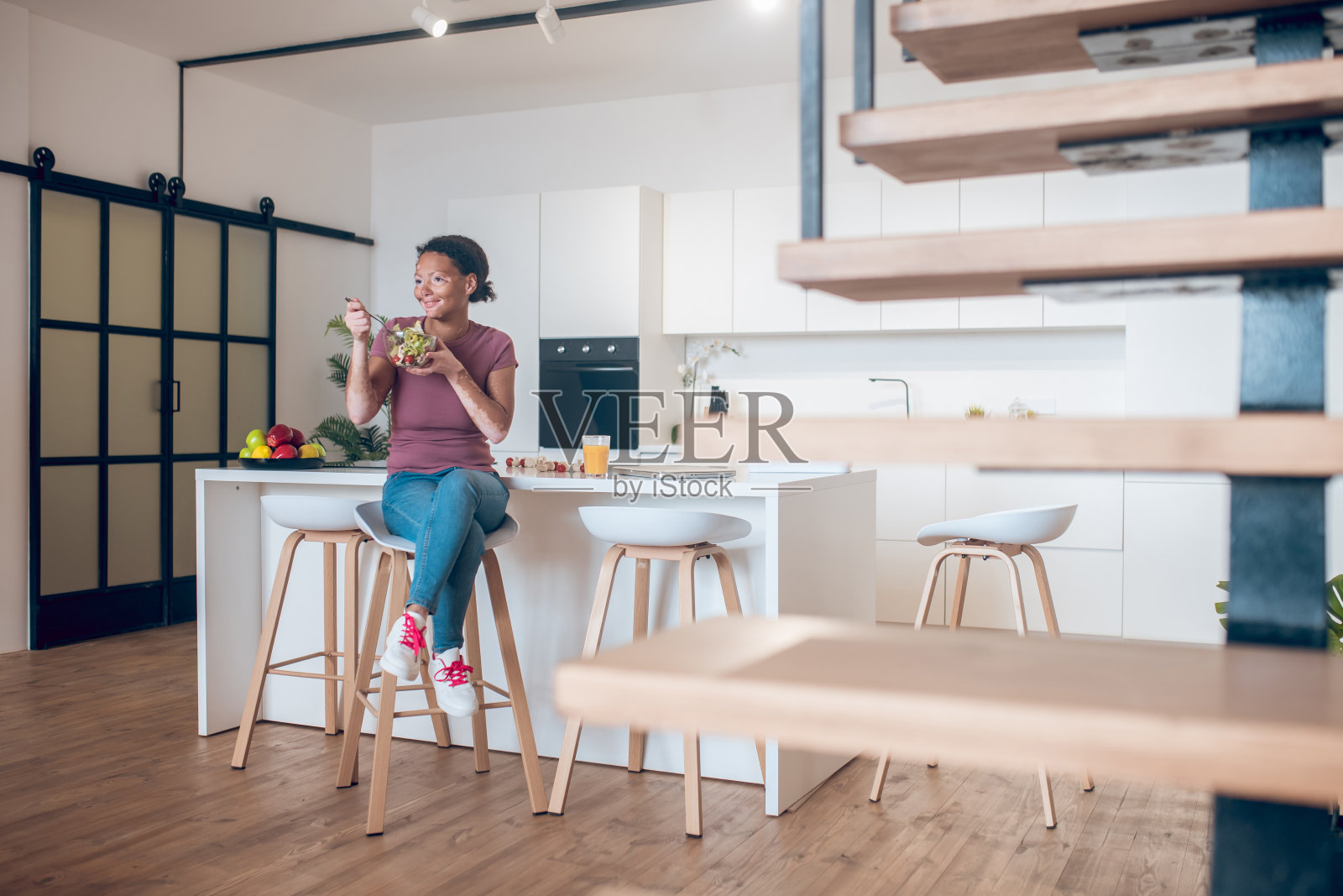 一个皮肤黝黑的女人坐在厨房里吃着沙拉照片摄影图片