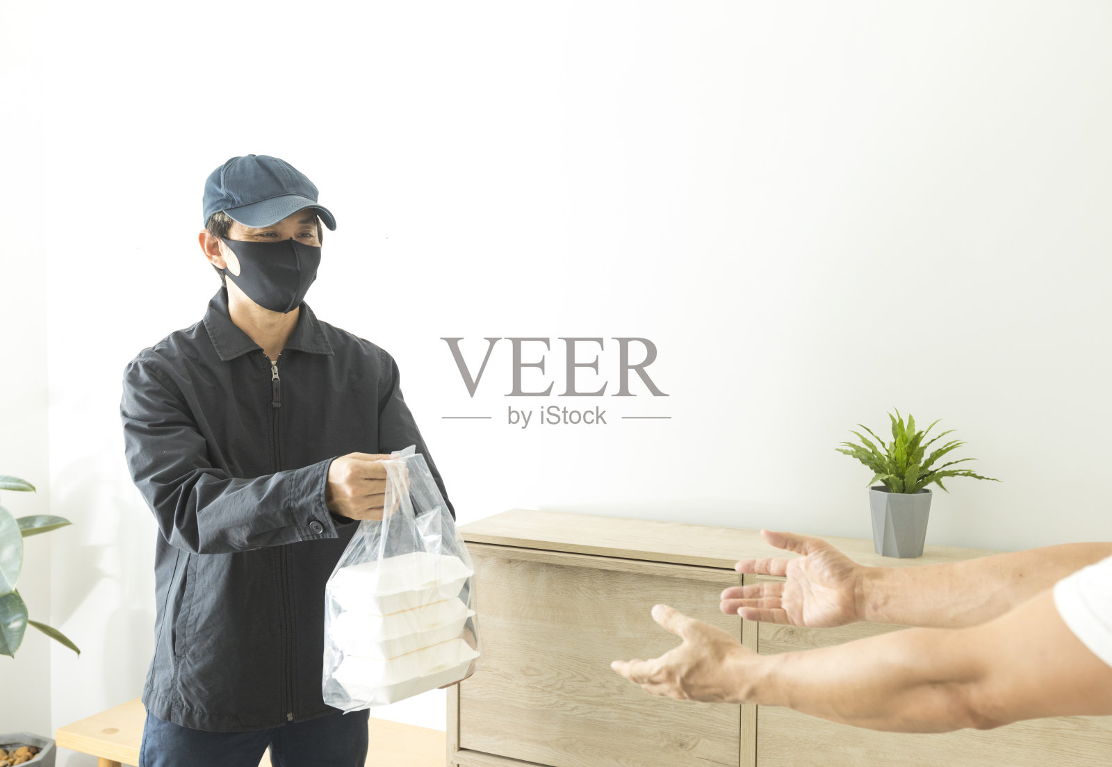 COVID-19爆发期间，一名亚洲快递员拿着一袋新鲜食品给顾客。照片摄影图片