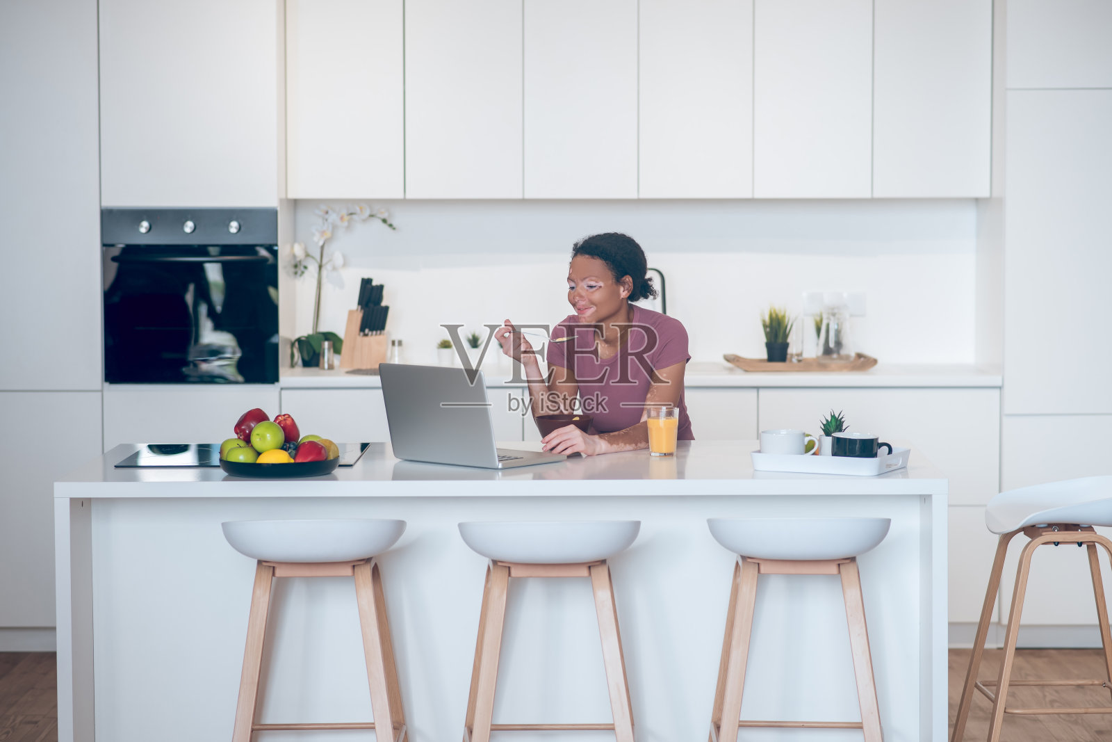 一个皮肤黝黑的年轻女子在家里吃早餐，在笔记本电脑上看东西照片摄影图片