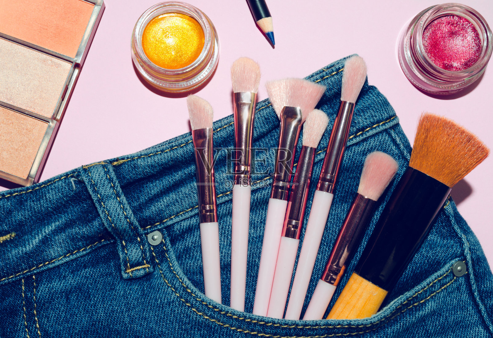 化妆刷眼影，在蓝色牛仔裤的口袋里，收集专业的化妆品配件在粉红色的背景。创意时尚的概念。收集化妆品化妆，俯视图。照片摄影图片