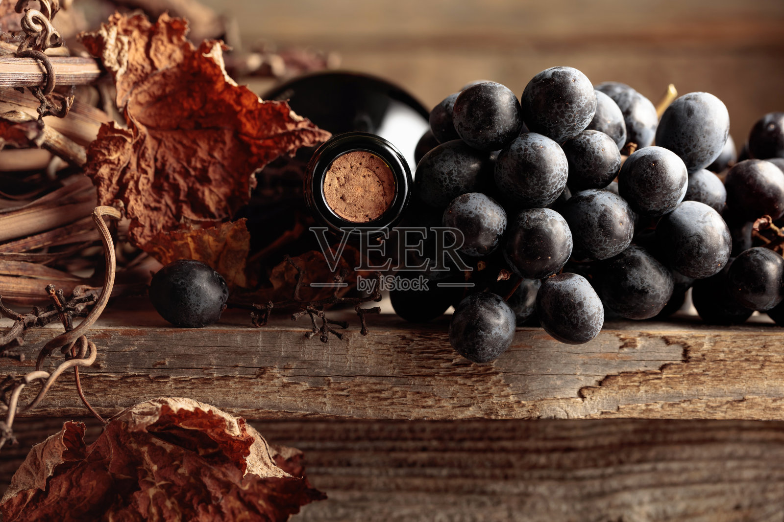 旧木桌上放着一瓶红酒、葡萄和干葡萄藤。照片摄影图片