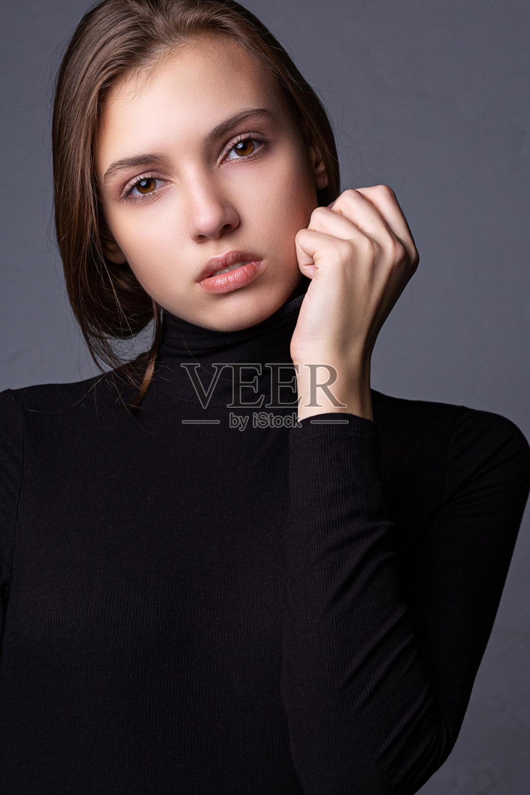 可爱的褐发女孩与裸妆在灰色的墙上摆姿势的测试拍摄照片摄影图片