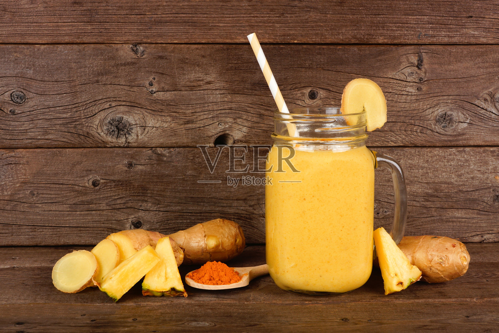 菠萝，姜黄，生姜冰沙在一个泥瓦匠罐，以深色木材为背景与配料。照片摄影图片