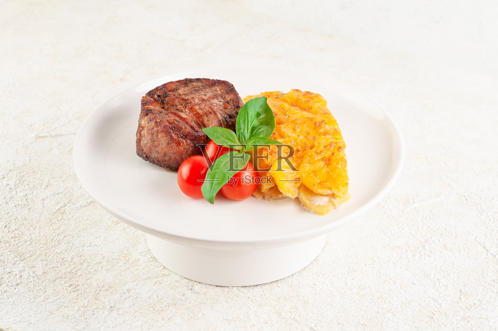 菲力牛排配烤土豆，芝士，圣女果和罗勒。特写镜头。光背景。照片摄影图片