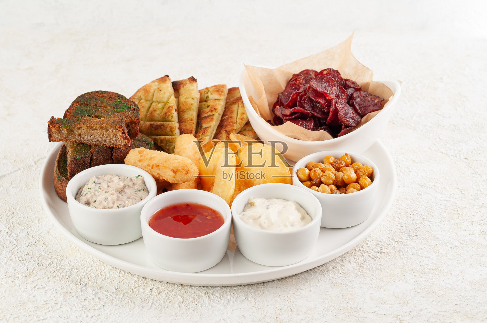 一套啤酒小吃。面包丁，皮塔饼，熏香肠和鸡块。配三种酱汁。放在一个白色的盘子里。光背景。照片摄影图片