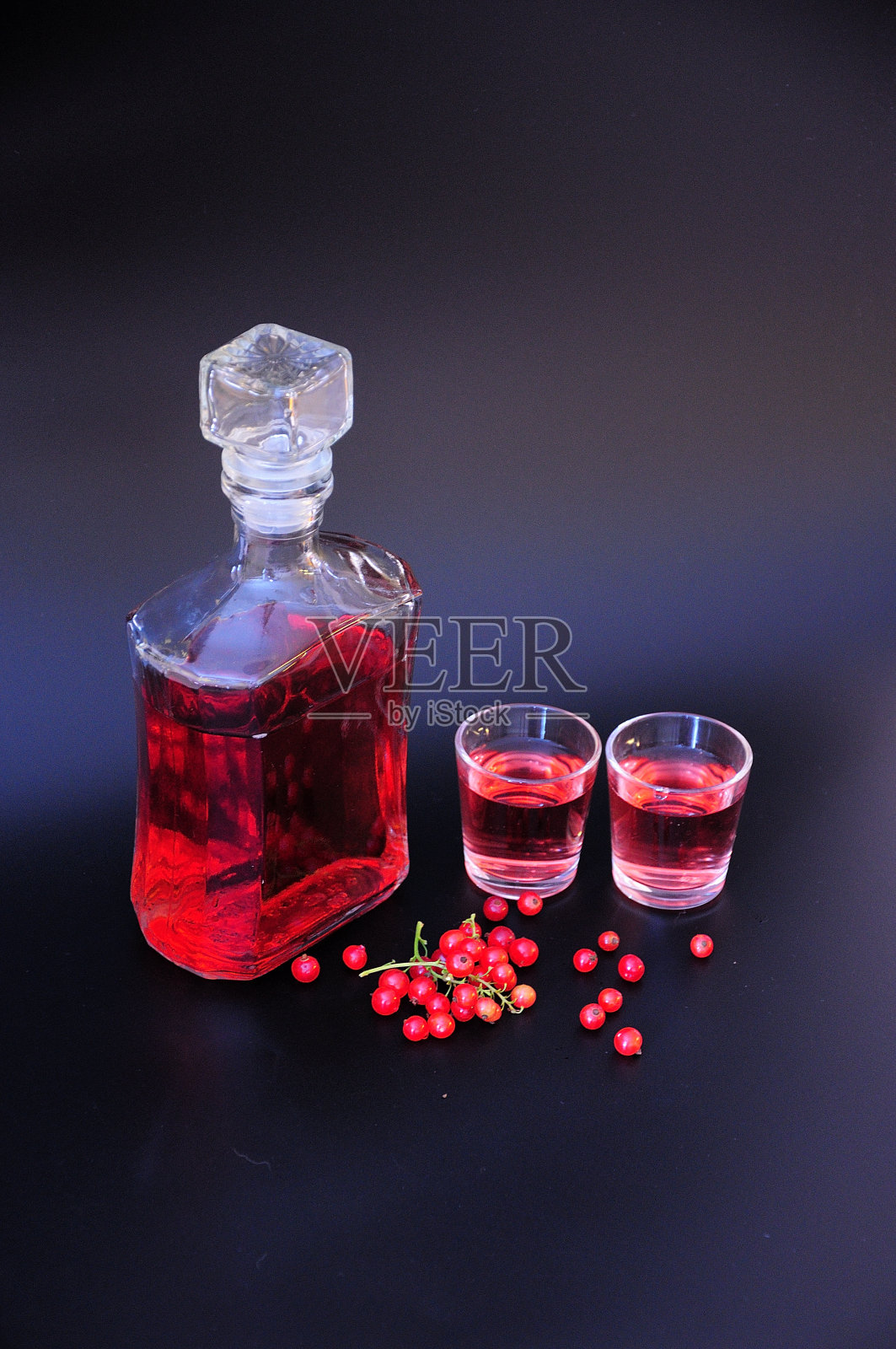 红醋栗利口酒，瓶子和玻璃杯与酒精饮料，旁边的一束成熟的浆果在一个黑色的背景。照片摄影图片