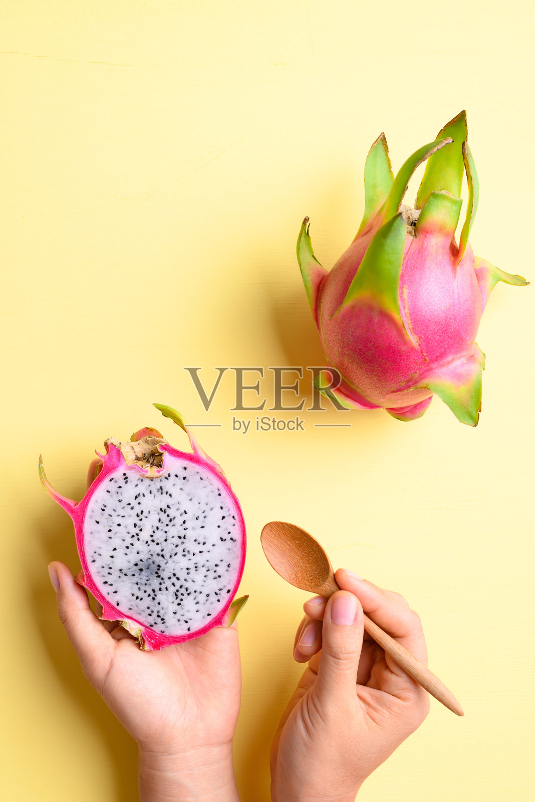 火龙果手拿着吃在黄色的背景上照片摄影图片