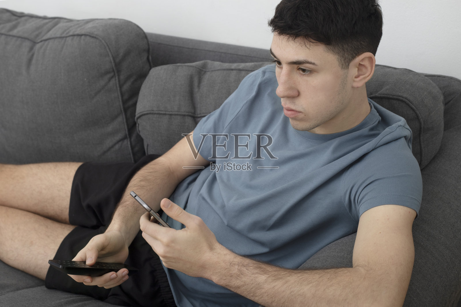 男孩躺在沙发上，拿着电视和手机照片摄影图片