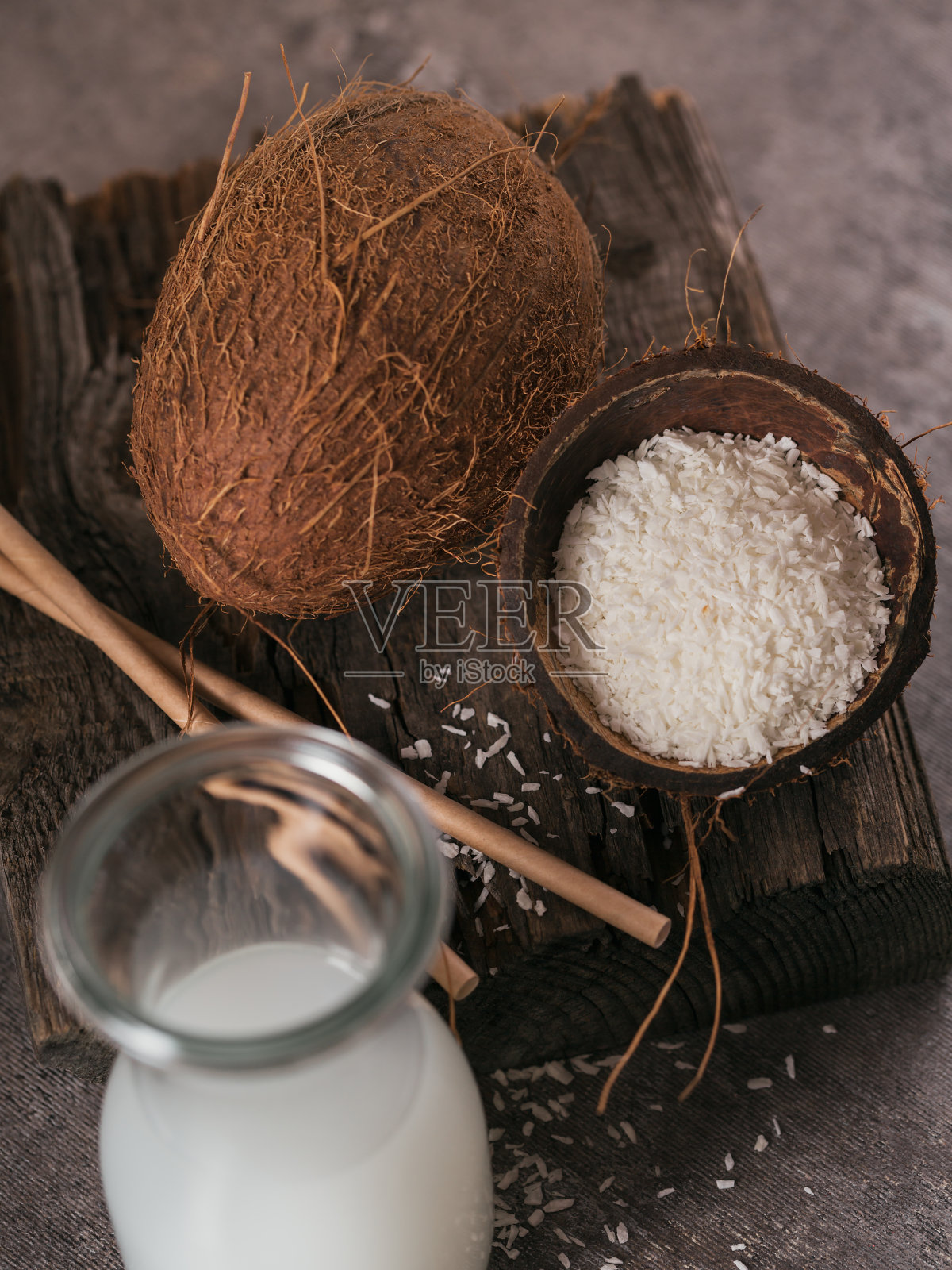 一瓶椰素牛奶，吸管，整个椰子和薄片在一个深色的背景。健康的生活方式的概念。照片摄影图片