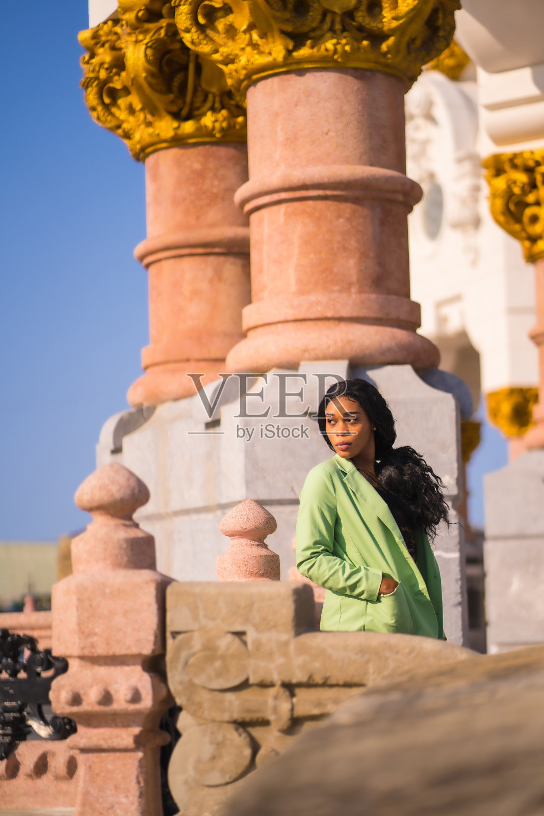 一个年轻的非洲黑人女孩的生活方式与美丽的绿色套装。游客坐在河柱上向左看照片摄影图片