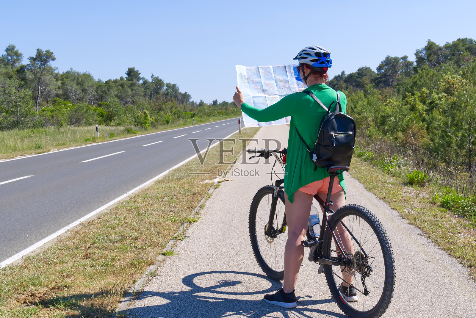 女游客戴着头盔骑在自行车上，在自行车道的十字路口检查地图照片摄影图片