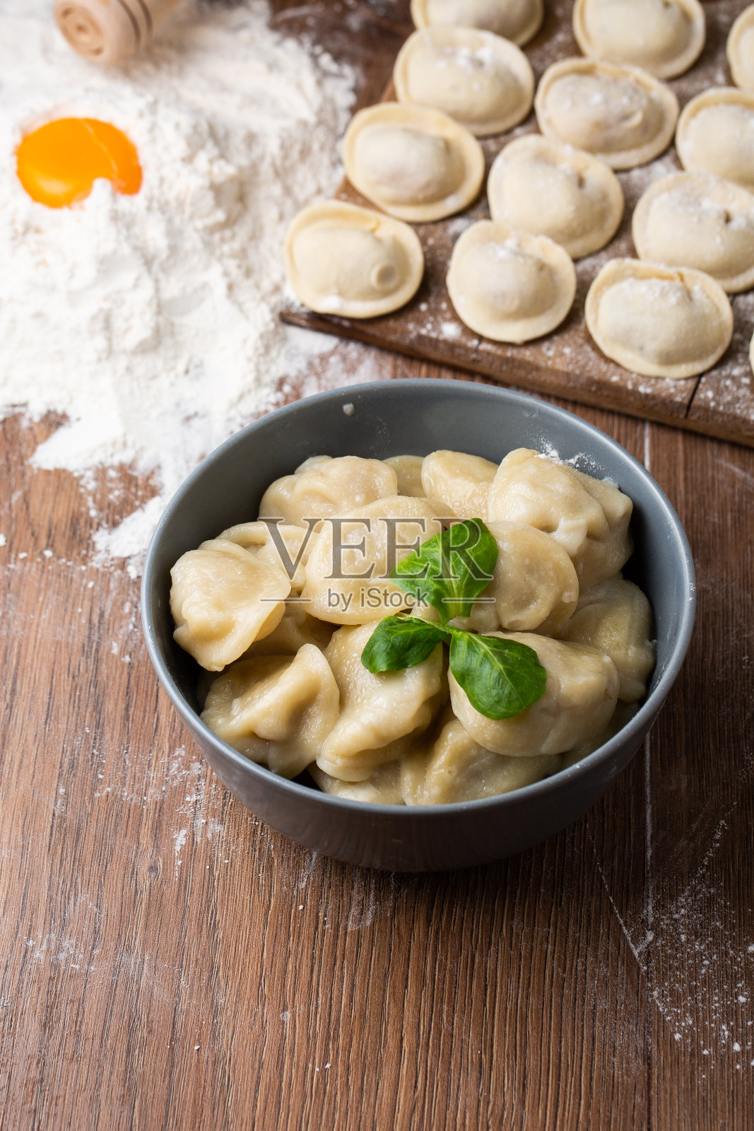 灰色的碗和准备好的俄罗斯肉馅，罗勒叶和木板，生饺子和肉末在桌上，撒上面粉。有选择性的重点照片摄影图片