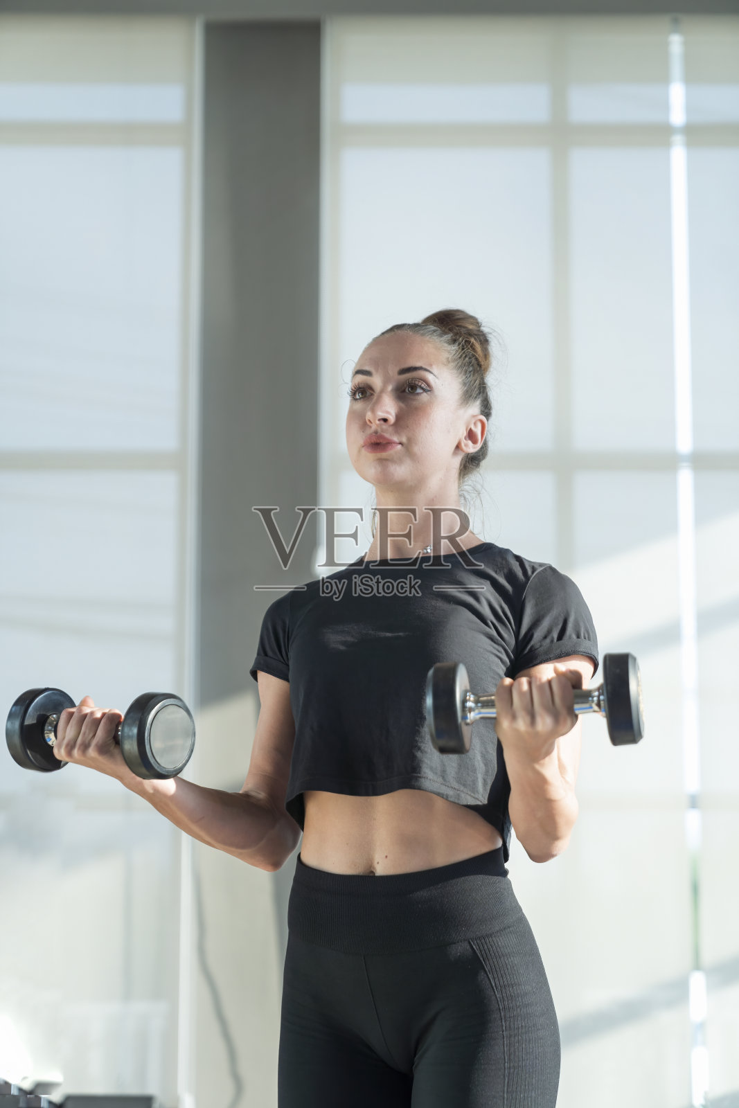 女人在玩哑铃锻炼肌肉。肌肉发达的年轻女性用哑铃锻炼。照片摄影图片