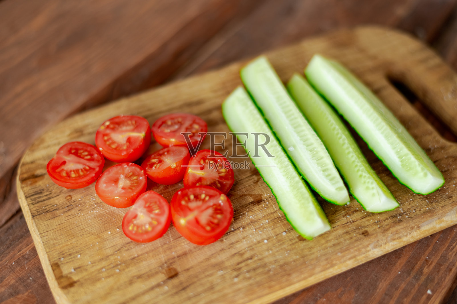 把樱桃番茄和黄瓜切成薄片放在木板上。准备做沙拉。素食。照片摄影图片