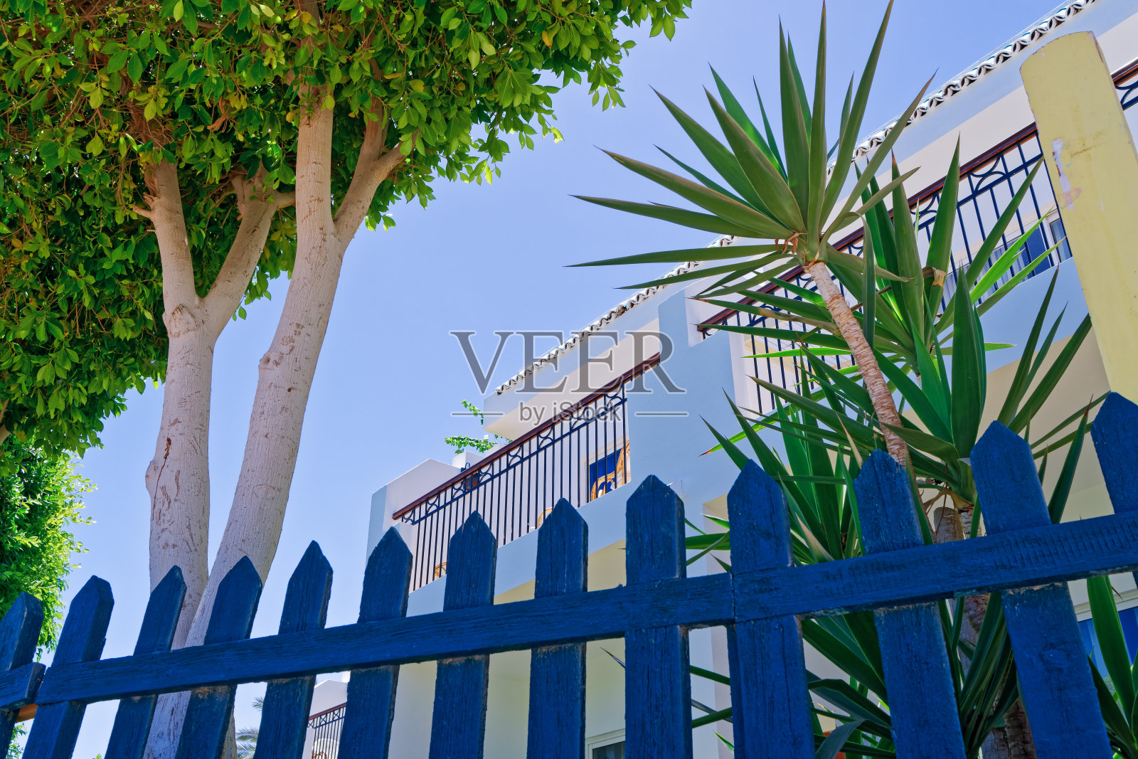 花园与带白色墙壁和阳台的现代建筑，坐落在蓝色木栅栏后面。度假概念，在度假村休闲。照片摄影图片